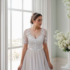 a woman standing in front of a window wearing a wedding dress