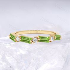 a yellow gold ring with green and white stones on the sides, sitting on top of some ice