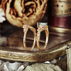 two gold wedding rings sitting on top of a table next to a vase with flowers