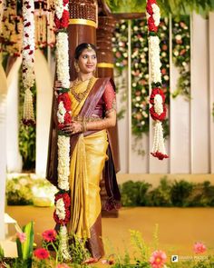 a woman in a yellow sari standing next to a pole with flowers on it