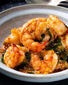 a white bowl filled with cooked shrimp and greens