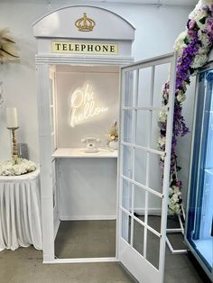 a white phone booth with flowers on the table and an open door that says telephone