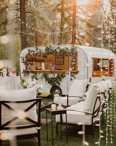 an rv is parked in the woods with white furniture and lights strung from it's windows