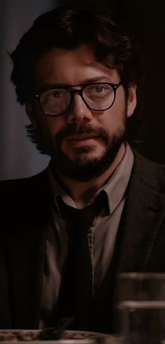 a man wearing glasses and a suit looks at the camera