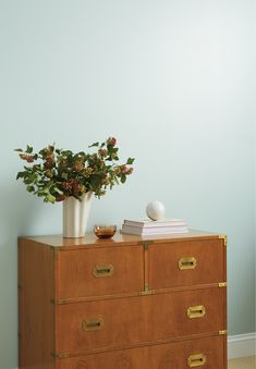 a vase with flowers on top of a wooden dresser