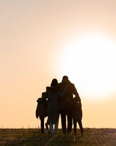 three people standing in the grass with their arms around each other as the sun sets