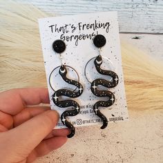 a pair of black and white snakes dangling from hoop earrings on top of a card