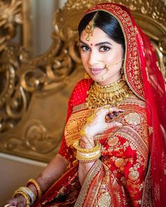 a woman in a red and gold bridal outfit posing for the camera with her hands on her chest