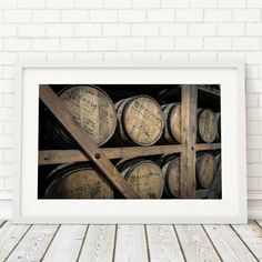 a framed photograph of wine barrels on a wooden floor in front of a brick wall