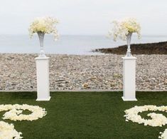 two tall vases with flowers are on the grass by the water at this beach wedding