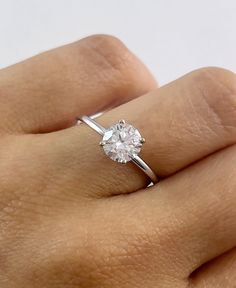 a woman's hand with a diamond ring on top of her finger, showing the center stone