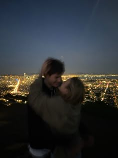 a man and woman standing next to each other in front of a city at night