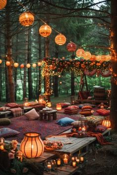 an outdoor seating area with lanterns, pillows and blankets on the ground in front of trees