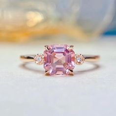 an engagement ring with a pink sapphire and diamonds on the side, sitting on a white surface