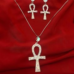 Our Ankh earring and necklace set is a stunning fusion of timeless symbolism and modern craftsmanship, meticulously crafted to embody the essence of elegance and mystique. At the heart of each piece lies the iconic Ankh symbol, revered in ancient Egyptian culture as a symbol of life and eternity. Sculpted with precision from luminous silver white mica, every Ankh pendant emanates a celestial glow, reminiscent of moonlit whispers on a tranquil night. Enveloped in hand-poured resin, the Ankh is lovingly encased, preserving its significance and beauty for generations to come. Delicate veins of silver leaf delicately adorn the edges, enhancing the ethereal allure of the design, while tiny rhinestones add a touch of celestial sparkle, reminiscent of stars scattered across a velvet sky. The earr Crystal Jewelry Sets For Gifts, Silver Hand Set Pendant Jewelry Sets, Symbolic Metal Jewelry For Formal Occasions, Symbolic Nickel-free Teardrop Jewelry, Symbolic Silver Jewelry With Matching Earrings, Elegant Ankh-shaped Metal Jewelry, Silver Crystal Jewelry Set As Gift, Crystal Jewelry With Matching Earrings For Gifts, Silver Crystal Jewelry Set For Gift