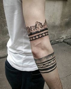 a man with a tattoo on his arm that has mountains and trees in the background