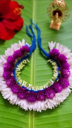 two flower leis on a green leaf next to a red and white flower crown