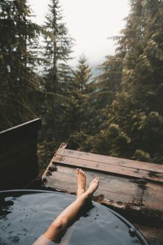 a person's feet in the water next to a hot tub with trees behind them