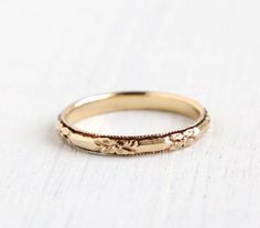 a gold wedding band with flowers on it, sitting on a white tableclothed surface