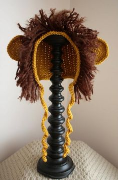 a crocheted hat is on top of a black lamp holder with a brown and yellow knitted animal's head