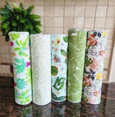 four rolls of fabric sitting on top of a counter next to a potted plant