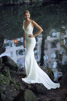 a woman in a white dress standing on rocks near water