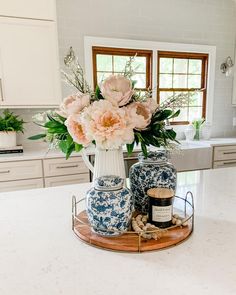 two vases with flowers on a tray in a white and blue themed kitchen area