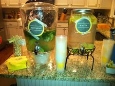 two large jars filled with liquid sitting on top of a kitchen counter next to glasses