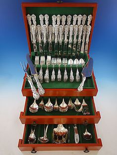 an assortment of silverware is displayed in a wooden case with green trays and handles