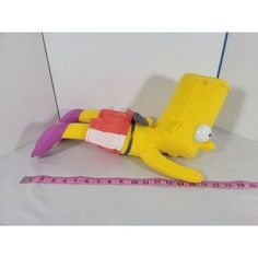 a yellow stuffed toy laying on its side next to a measuring tape and a white wall