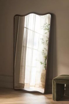 a large mirror sitting on top of a wooden floor next to a chair and window