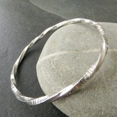 "This beautiful sterling silver bangle has been made from heavy gauge square silver wire, which I've textured with a sharp line pattern on two opposite sides. I've then twisted the entire length of wire, formed it into a bangle shape and soldered the ends, resulting in an unusual looking contemporary bangle. The twisted silver bangle has been given a highly polished finish which really catches the light. The bangle would look great worn as a stacking bangle with your other favourites - see the s Sterling Silver Bangle With A Modern Twist, Silver Bangle With A Modern Twist, Hammered Sterling Silver Bangle Bracelet, Twist Jewelry, Textured Bracelet, Twisted Bangle, Modern Jewellery, Line Texture, Bangles Making