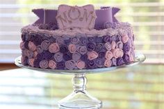 a purple and pink cake sitting on top of a glass plate next to a window