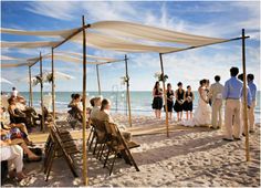 a group of people standing on top of a sandy beach next to the ocean with white umbrellas