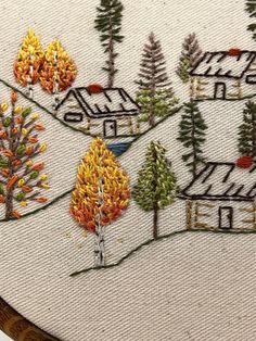 a close up of a cross stitch on a piece of cloth with trees and houses