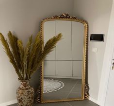 a large mirror sitting on top of a counter next to a vase filled with grass