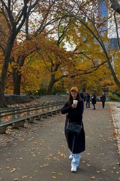 a woman walking down a path holding a cup of coffee in her hand and looking at the camera