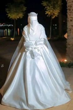 a white wedding gown on display in front of palm trees at night with lights behind it