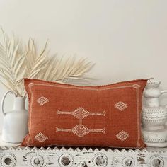 an orange pillow sitting on top of a table next to a vase and potted plant