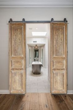 an open door leading to a bathroom with a tub in the center and wooden floors