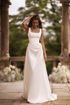 a woman in a white dress is posing for the camera with her hand on her head