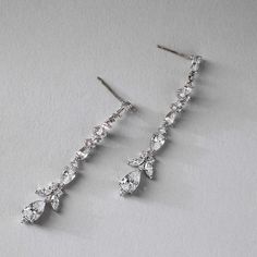 two pairs of diamond drop earrings on a white surface with one earring dangling from the side