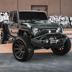 a black jeep parked in front of a building with graffiti on the wall behind it