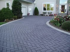 a driveway with brick pavers and flowers in the front yard, leading to a large house