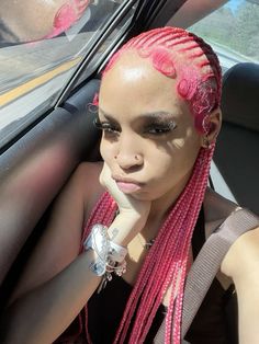 a woman with pink hair sitting in the back seat of a car, looking at the camera