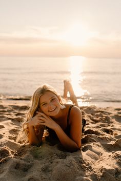 a woman laying on top of a sandy beach next to the ocean with her feet in the sand