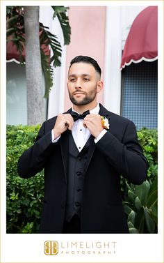 a man in a tuxedo adjusts his bow tie while posing for the camera