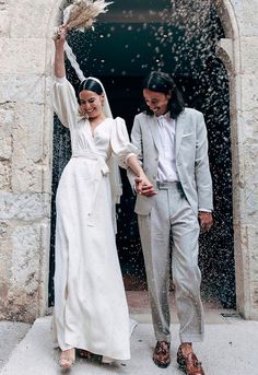 a man and woman in wedding attire walking out of an open doorway with rice falling from their hands