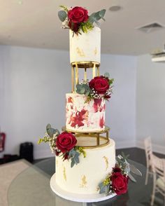 a three tiered cake with red roses on top is sitting on a glass table