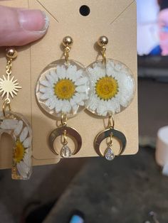 a pair of earrings with daisies and crescents hanging from the earring hooks